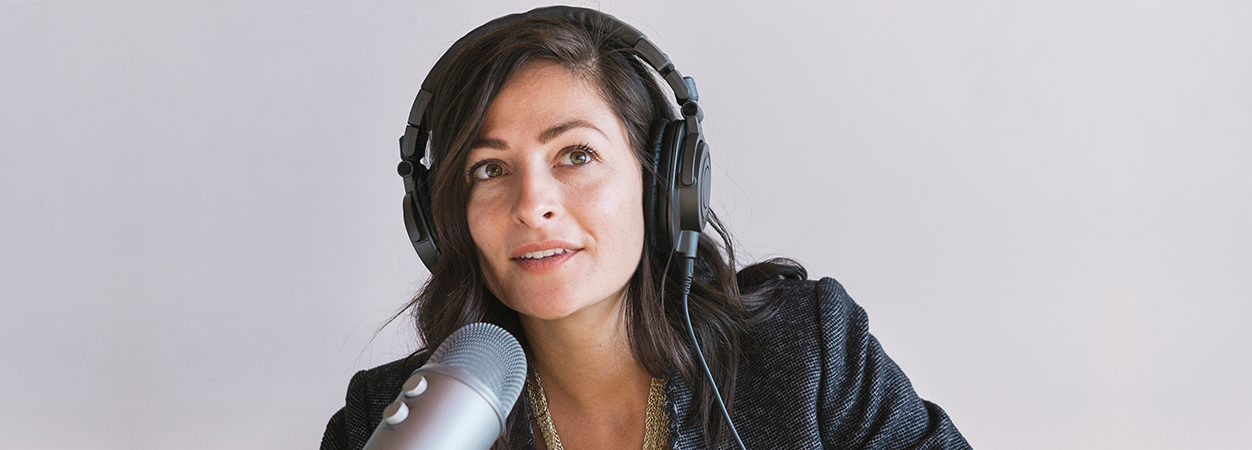 A woman with headphones and a microphone conducts a podcast.