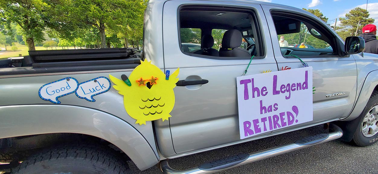A passenger truck with two signs and a bird wearing star glasses hanging on its side.