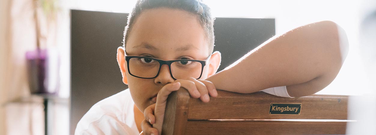 A child wearing glasses stares blankly into the camera.