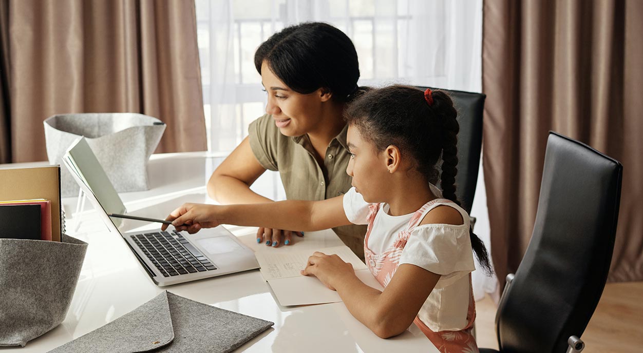 A mom helps her daughter with homework at the laptop.