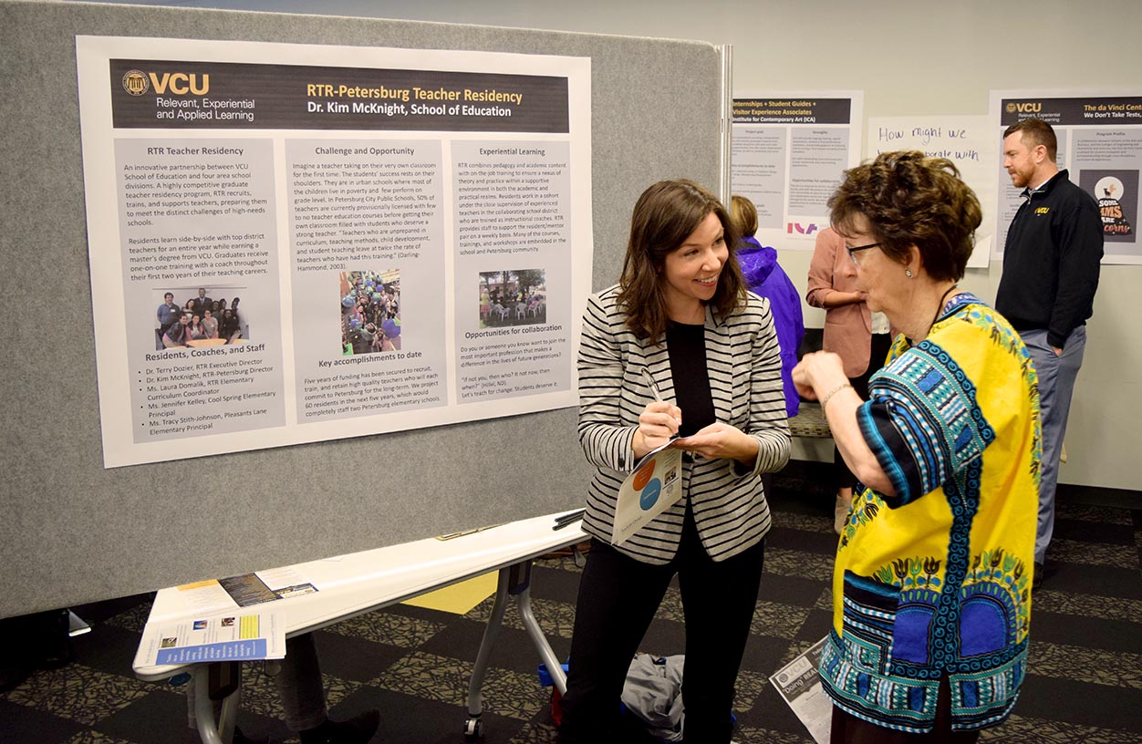 Dr. Kim McKnight, RTR-Petersburg director, helps a visitor to her booth at the VCU “Doing” REAL Poster Session & Showcase at the Grace and Broad Residence 2.