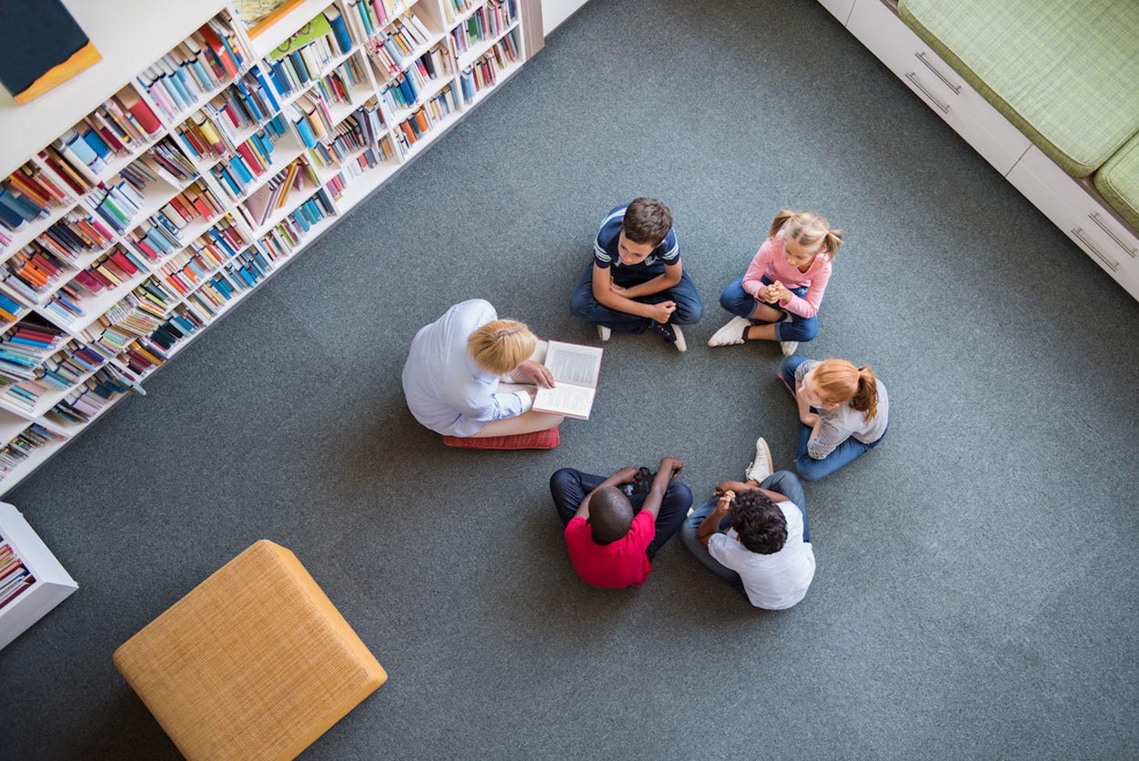 pre-school children and their teacher sitting in a circle in a library