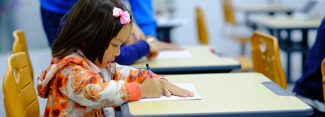 A child works on writing at a table in class. (Unsplash / Jerry Wang)